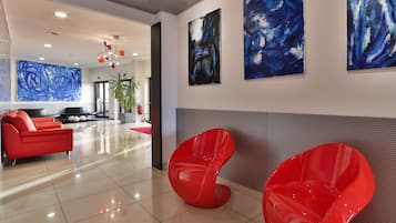 Un hall d’entrée moderne avec un canapé rouge, deux fauteuils rouges et des tableaux abstraits accrochés au mur.