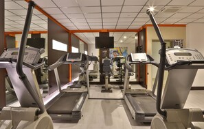 Une salle de sport équipée de tapis de course, de vélos elliptiques et d’un écran de télévision.