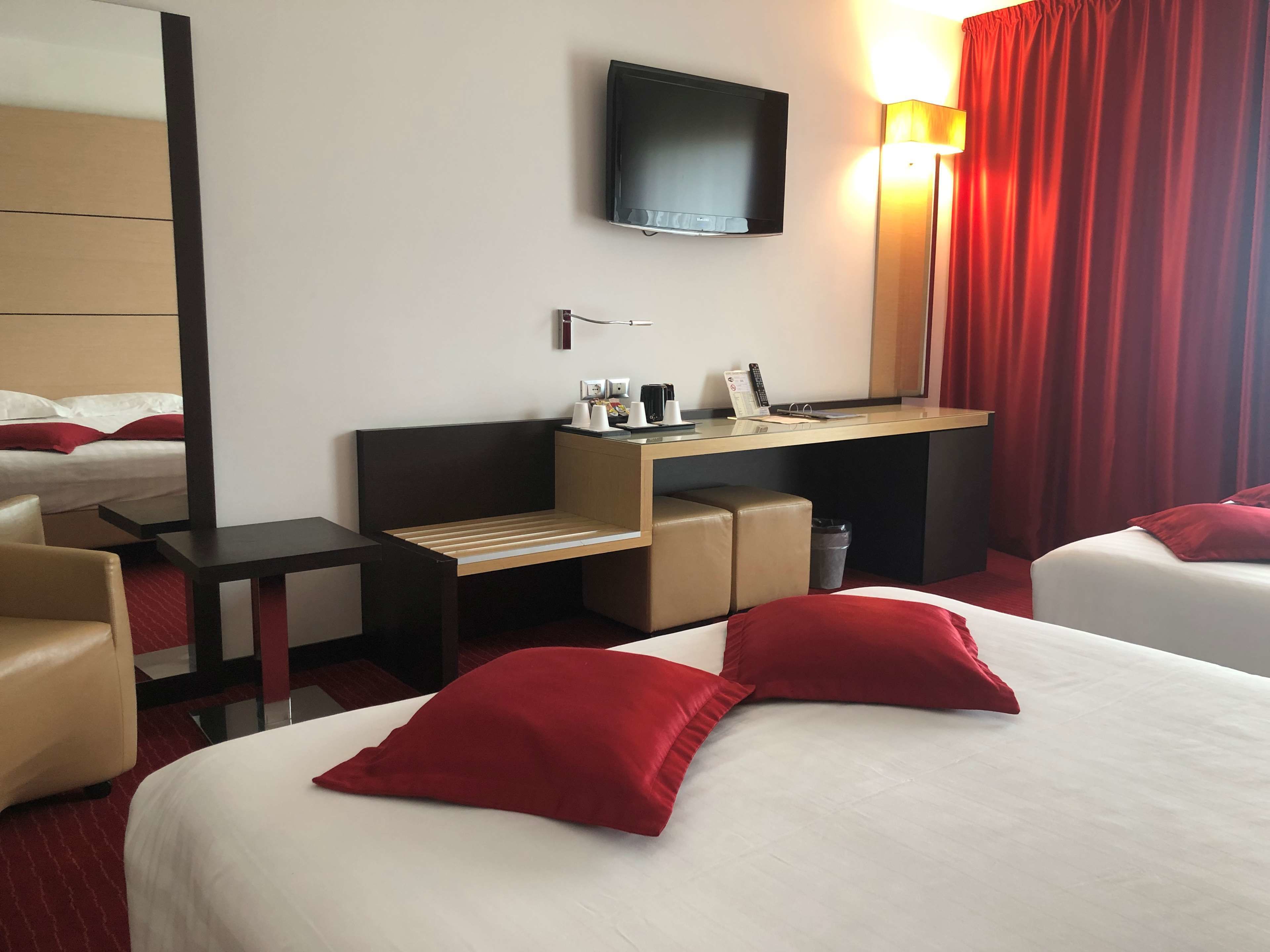 A hotel room with two beds, a desk, a TV, and a red curtain.
