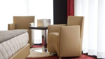 A hotel room with a bed, two armchairs, a small table, and a red carpet.