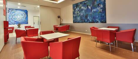 A modern dining area with red chairs and white tables, featuring abstract art on the walls.