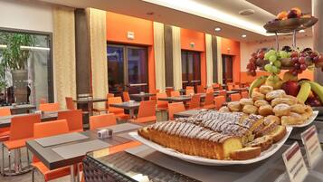 Un comedor moderno con sillas y mesas naranjas, una exhibición de frutas y un pastel grande.