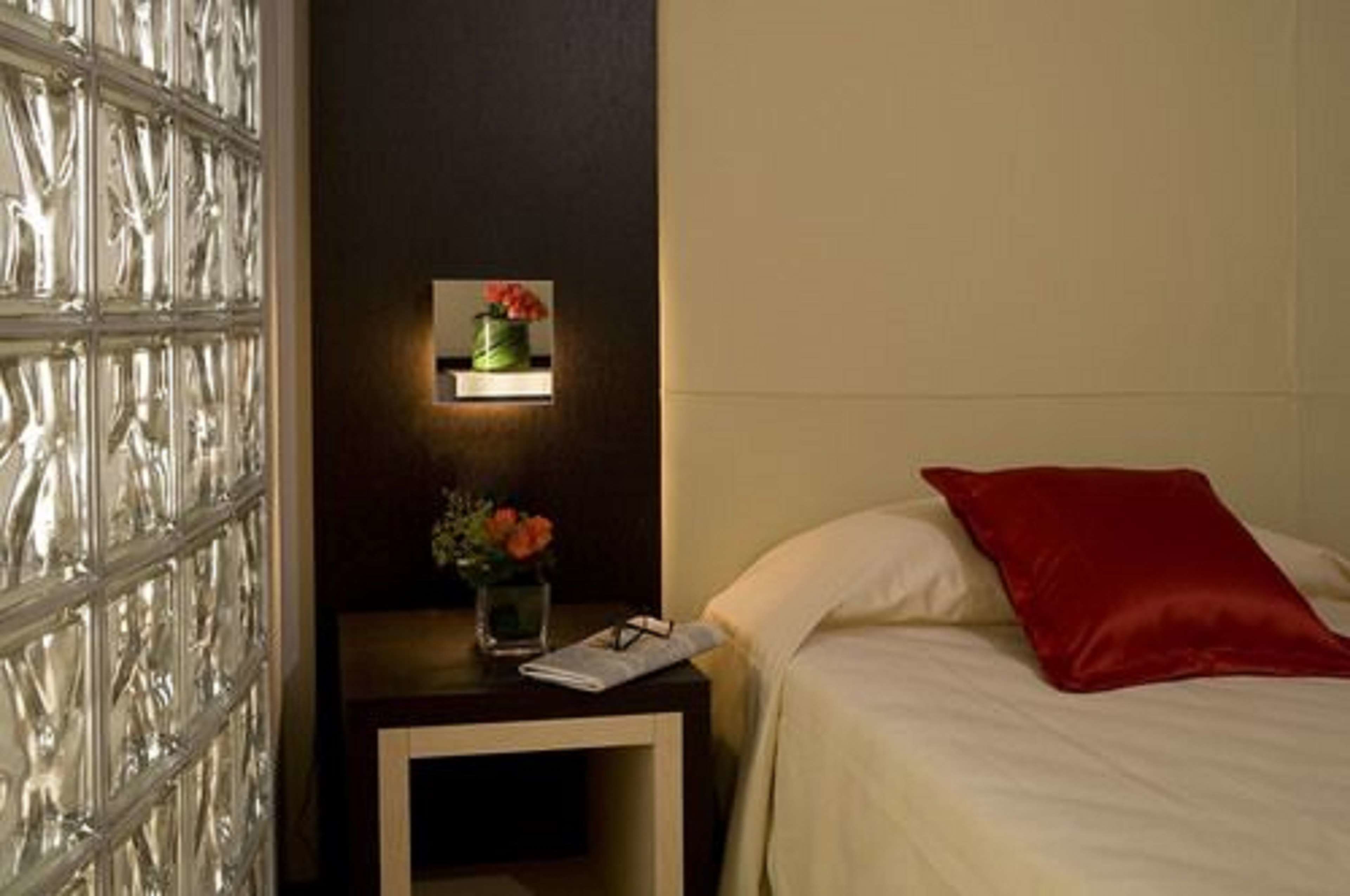Una habitación de hotel con una cama, una mesita de noche y una lámpara fijada a la pared.