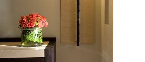 A reception desk with a vase of red flowers, a wall-mounted lamp, and a wooden floor.