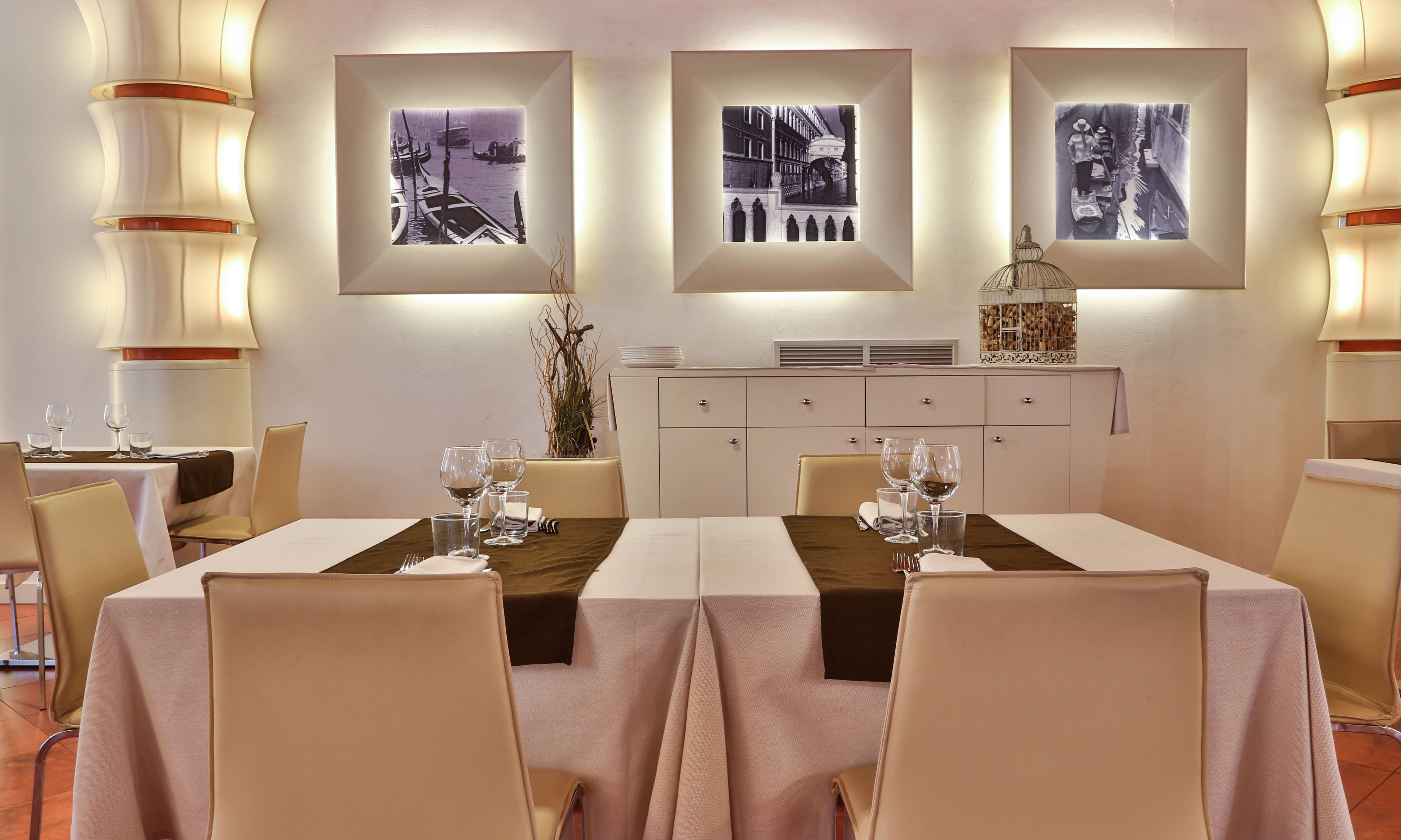 Un comedor con una mesa preparada para cuatro personas, rodeada de sillas. Hay fotografías en blanco y negro enmarcadas en la pared sobre la mesa.