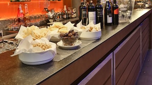 A bar area with shelves of liquor bottles, bowls of snacks, and a long counter.