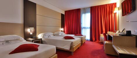 A hotel room with two beds, a desk, a chair, a TV, and a red carpet.