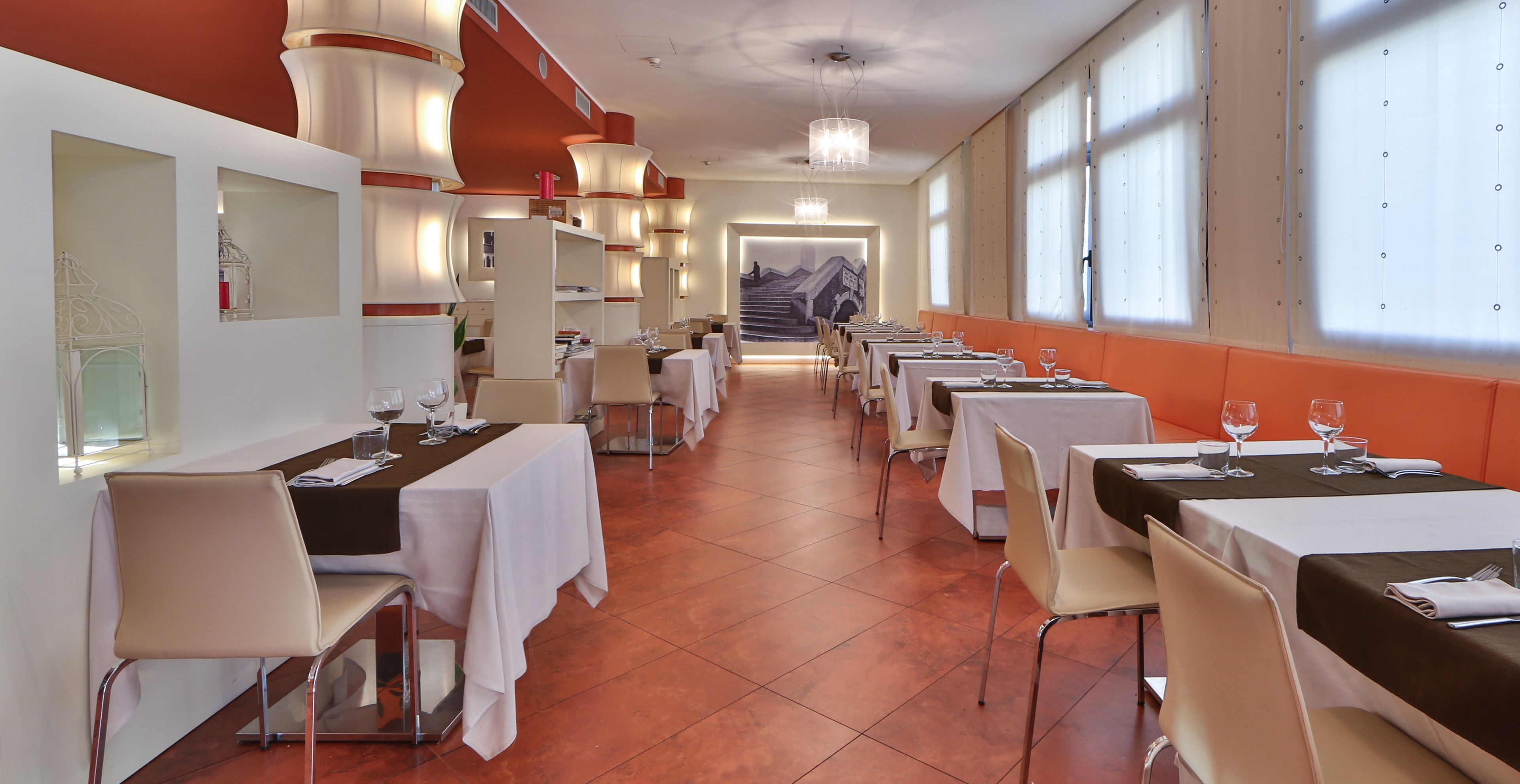 A restaurant with multiple tables and chairs, a tiled floor, and large windows.