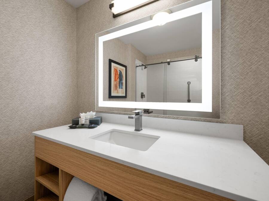 A modern bathroom with a white sink, wooden vanity, and a large mirror.
