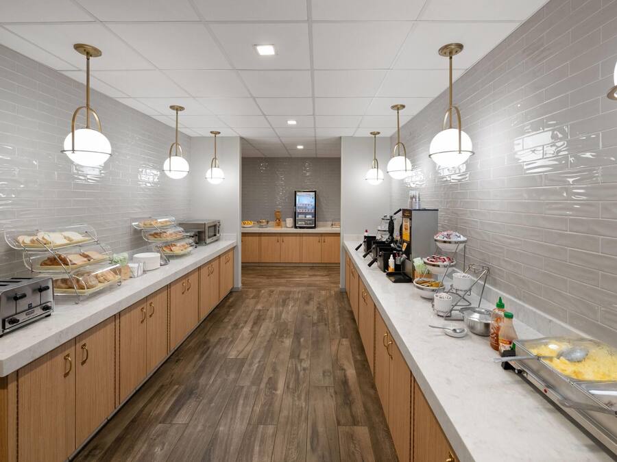 A modern kitchen with a long counter, food dispensers, a coffee machine, and a microwave.