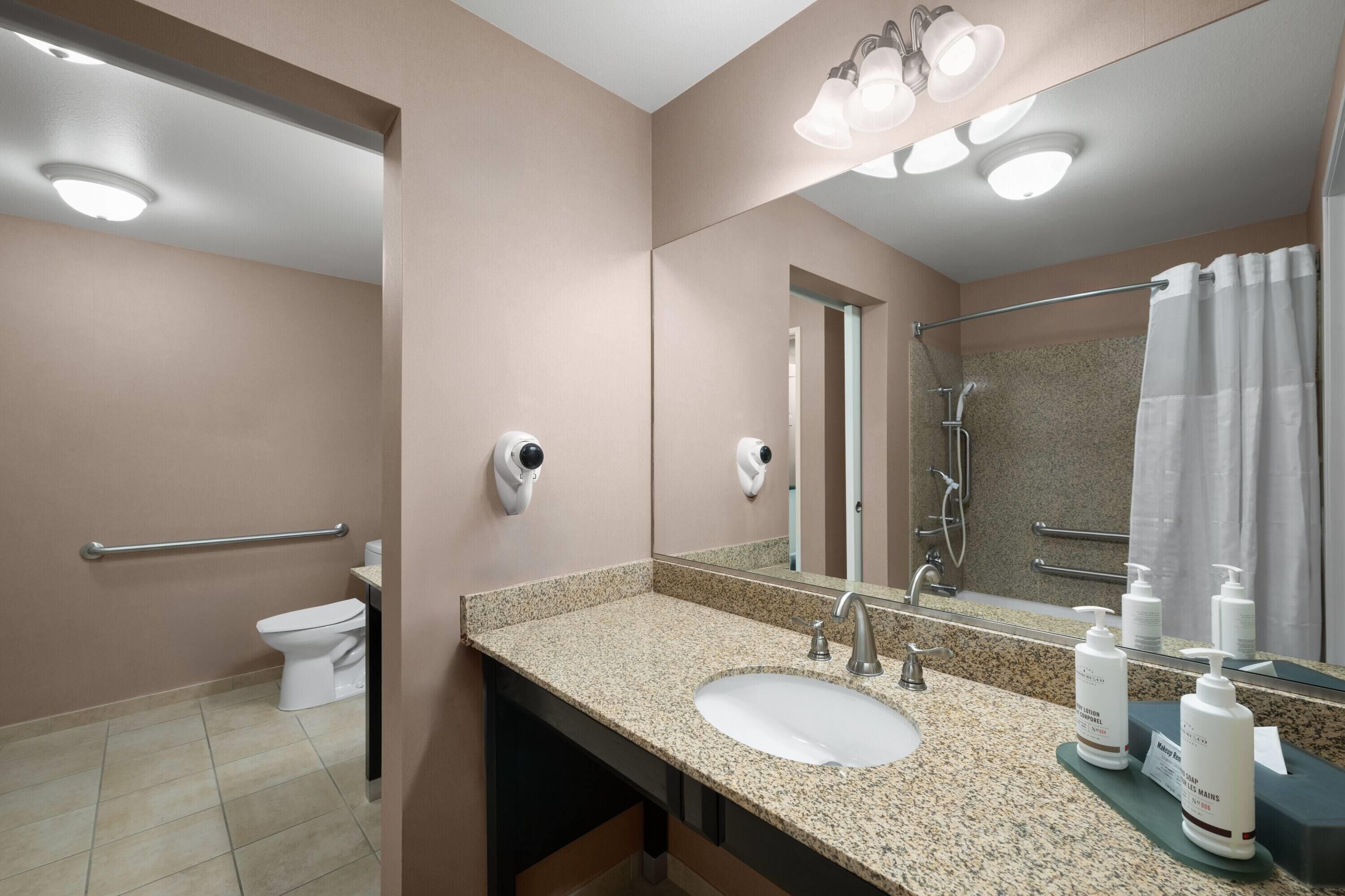 A modern bathroom with a granite countertop sink, a handheld showerhead, and a toilet.