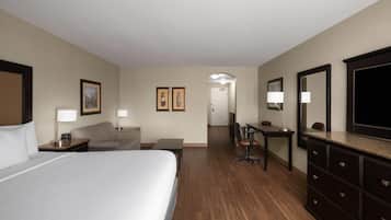 Una habitación de hotel con una cama grande, un escritorio, una silla, un aparador y una televisión.