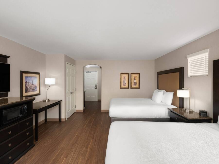 A hotel room with two beds, a desk, a TV, and a door leading to another room.