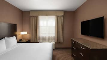 A hotel room with a large bed, a flat-screen TV, a nightstand with a lamp, a dresser, and a window with curtains.