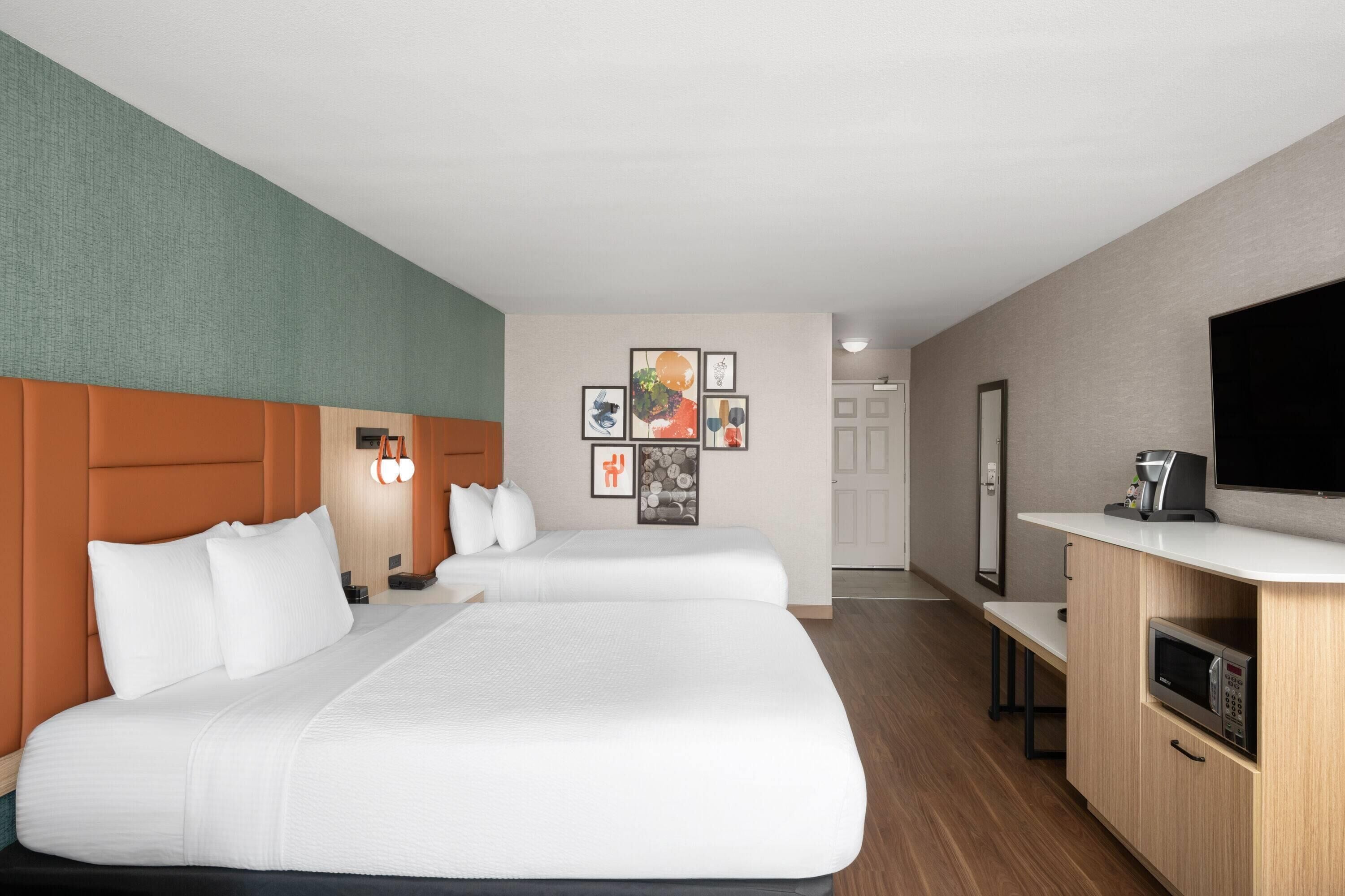 Habitación de hotel con dos camas, kitchenette, televisión de pantalla plana y obras de arte en la pared.