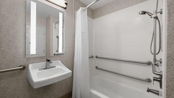 Un baño con lavamanos blanco, un espejo, ducha con puerta de vidrio y barras de apoyo.