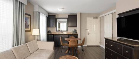 A modern living room with a sofa, a dining table with chairs, a TV, and a kitchen area in the background.