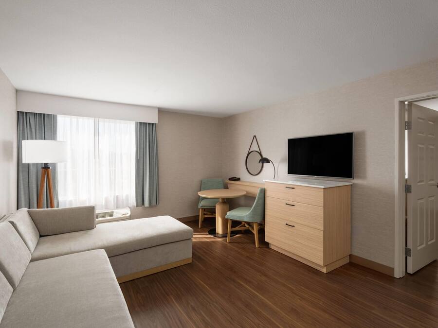 Una habitación de hotel moderna con sofá, escritorio, televisor y mesa de comedor.