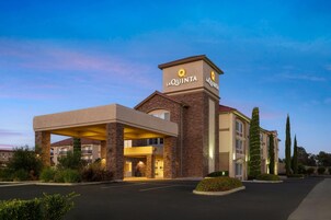 Hotel La Quinta con fachada de ladrillo, entrada cubierta y camino de acceso ajardinado.
