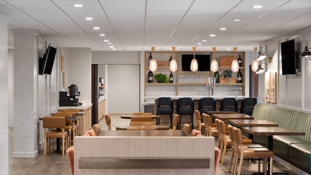 A modern restaurant with wooden tables and chairs, a central bar area, and a seating section with a green cushioned bench. - La Quinta Inn & Suites by Wyndham Paso Robles (Paso Robles)