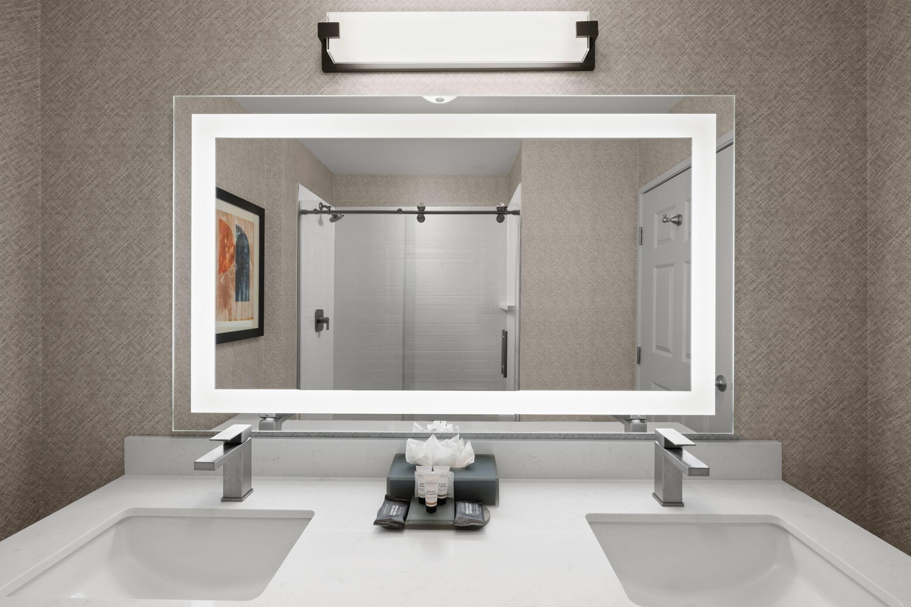 Ein modernes Badezimmer mit einem großen Spiegel, zwei Waschbecken und einer Dusche.