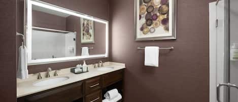 A modern bathroom with a double sink vanity, a large mirror, and a shower area.