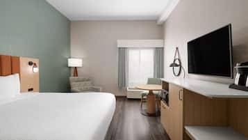 A hotel room with a large bed, a desk, a chair, a TV, and a lamp.