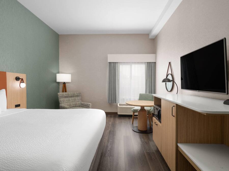 A hotel room with a large bed, a desk, a chair, a TV, and a lamp.