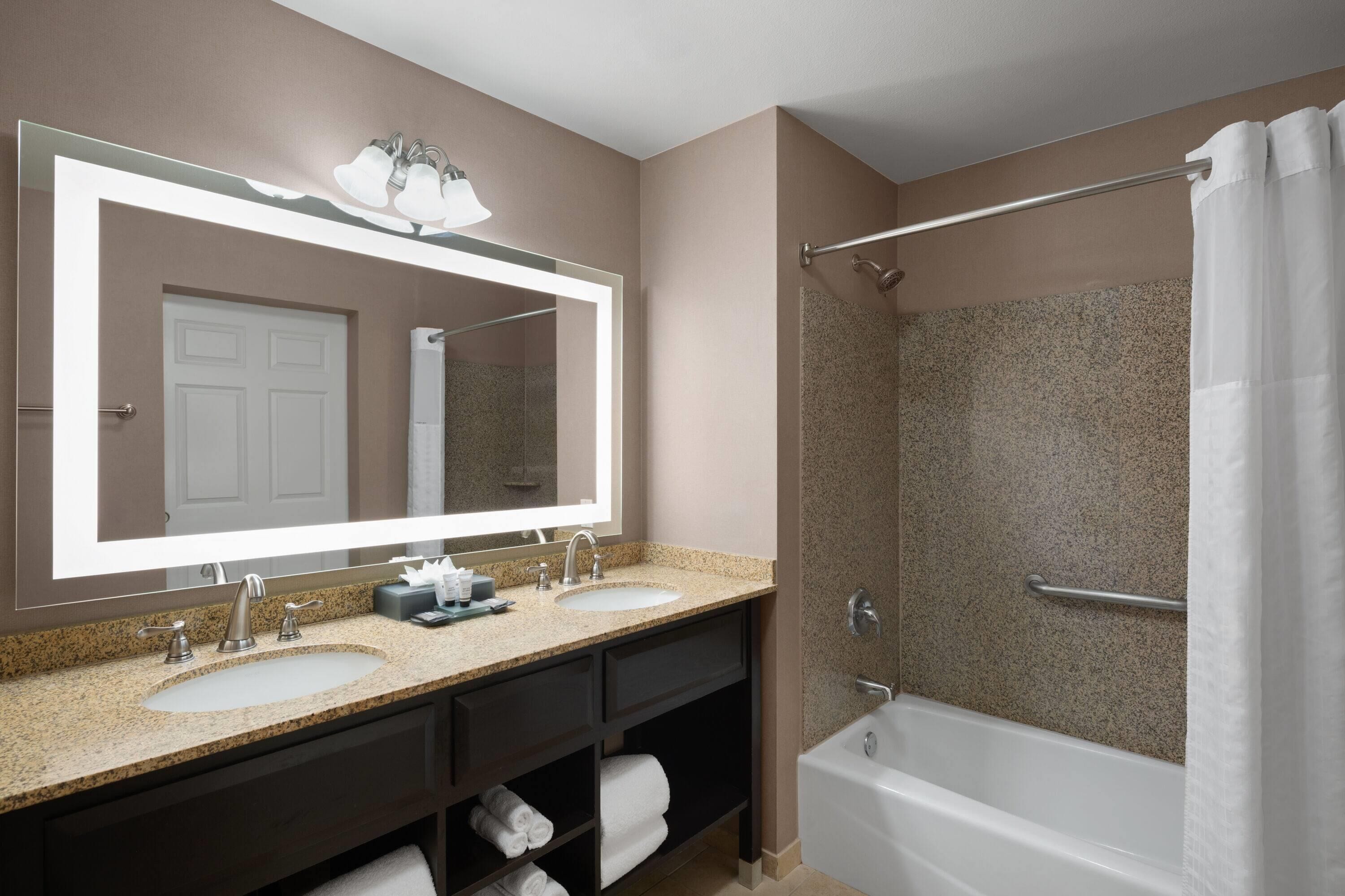 Een badkamer met een dubbele wastafel, een grote spiegel, een douche met glazen deur en een bad.