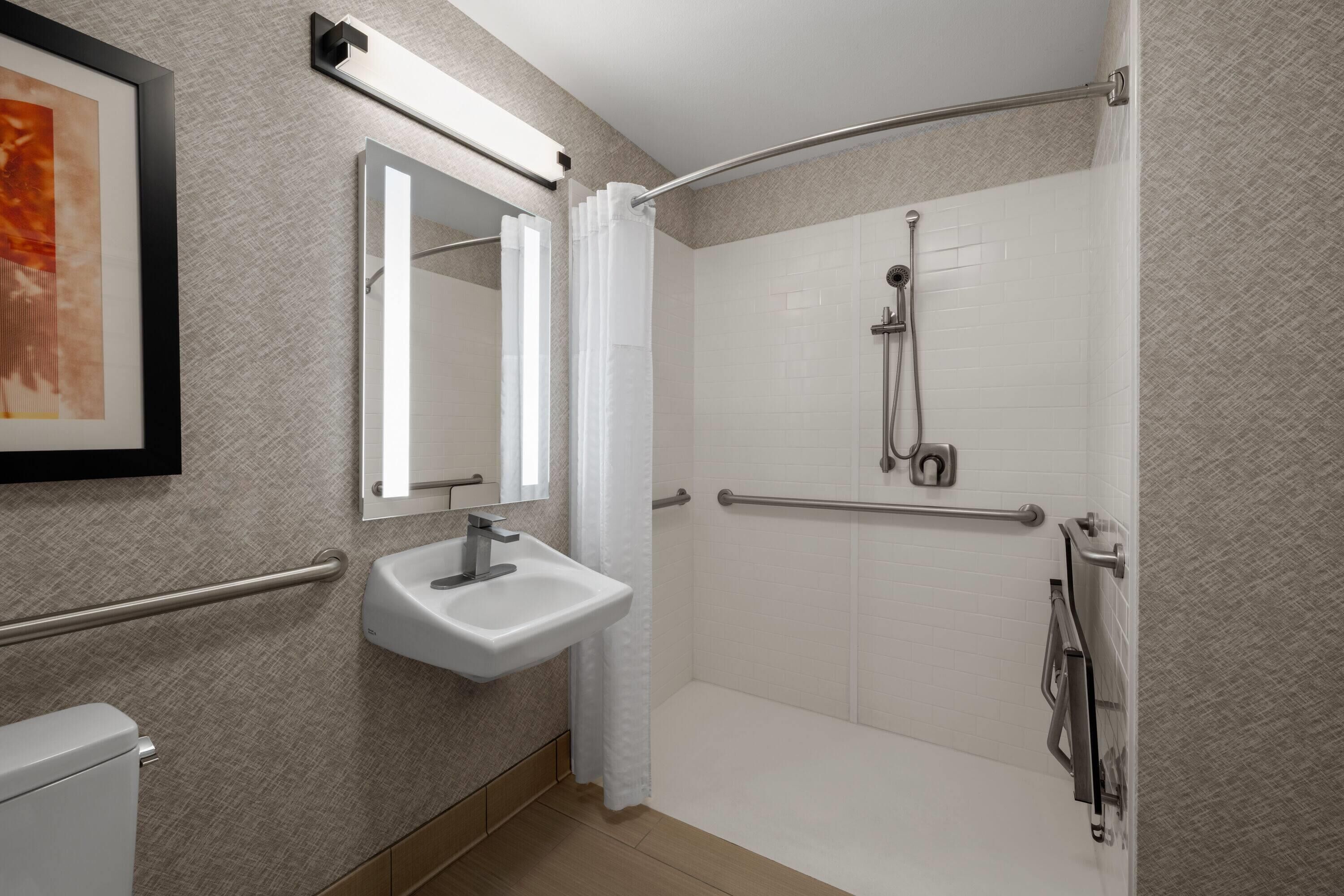 Casa de banho moderna com lavatório branco, espelho, chuveiro com barra de apoio e um quadro na parede.
