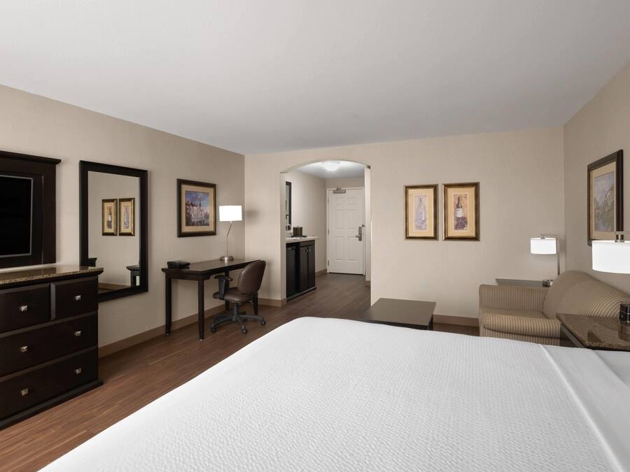 Una habitación de hotel con una cama grande, un escritorio con silla, un aparador, un televisor y cuadros en las paredes.