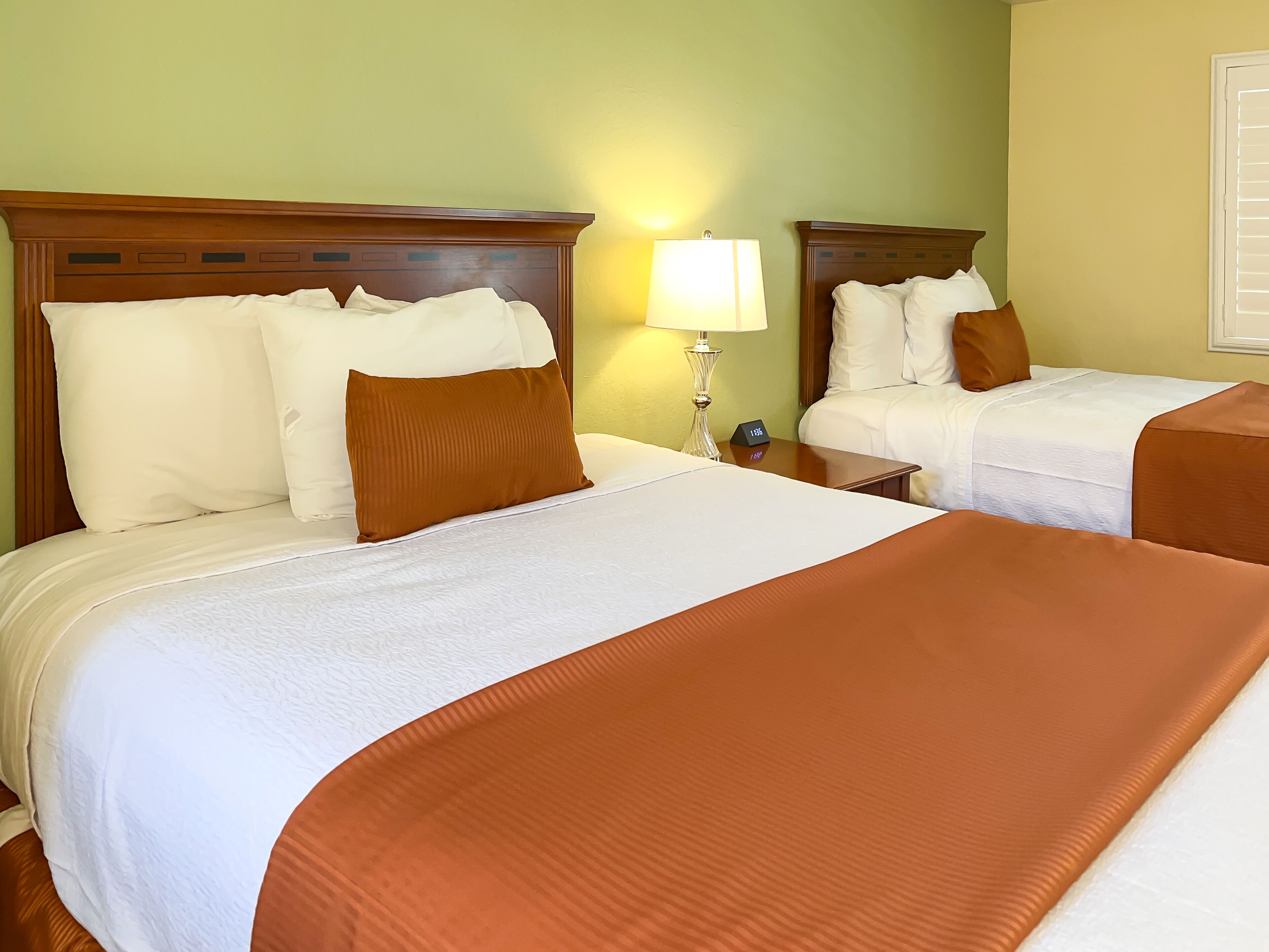 A hotel room with two beds, each with white and brown bedding, a nightstand with a lamp, and a clock displaying 1:35.