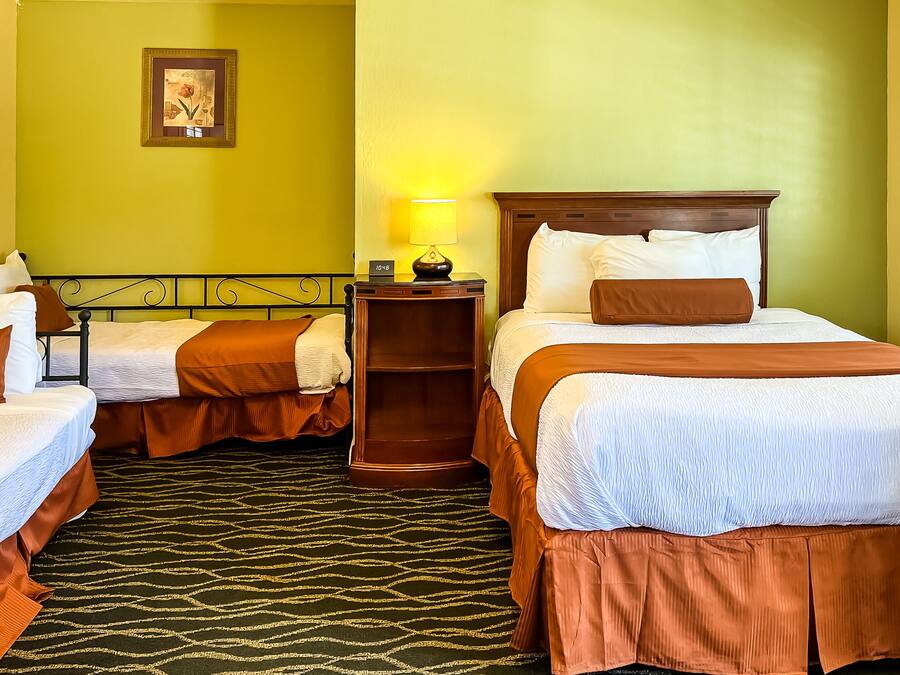 A hotel room with two single beds, a nightstand with a lamp, a wooden headboard, and a framed picture on the wall.