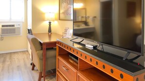 Habitación de hotel con escritorio de madera, televisor de pantalla plana, lámpara, silla y cómoda.
