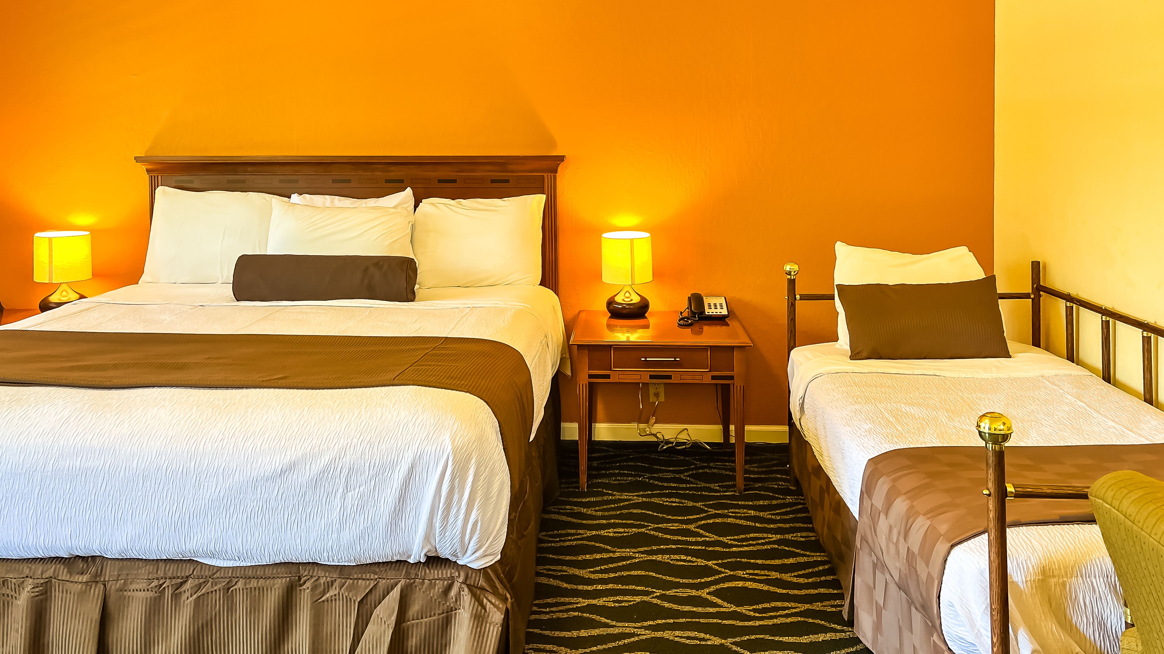 A hotel room with two beds, a nightstand, and a lamp.