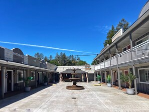 Une cour avec une fontaine, entourée de bâtiments portant les enseignes « Bureau de poste » et « Banque ».