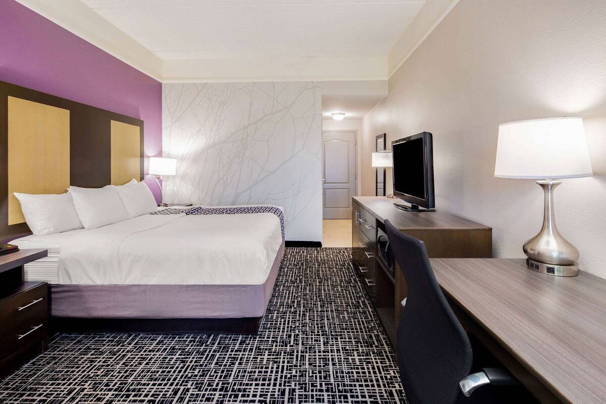 A hotel room with a bed, a desk, a TV, and a lamp.