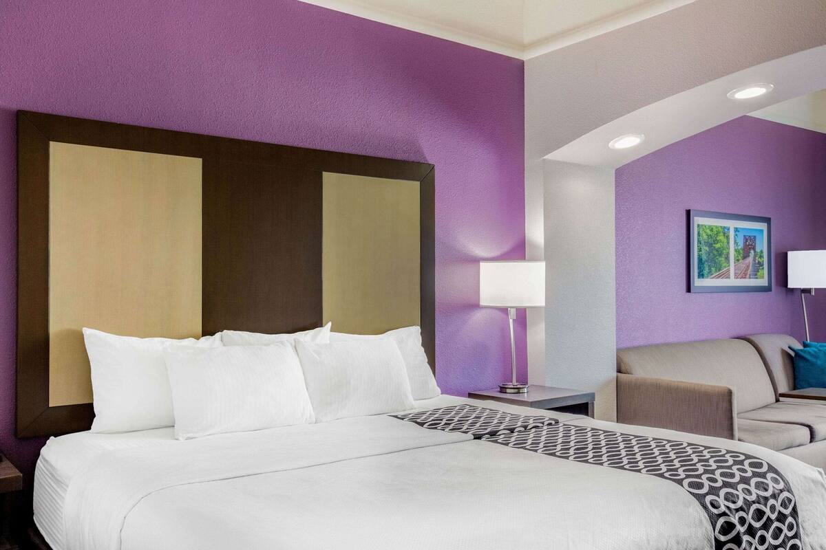 A hotel room with a large bed, a nightstand, a desk, a chair, and a painting on the wall.