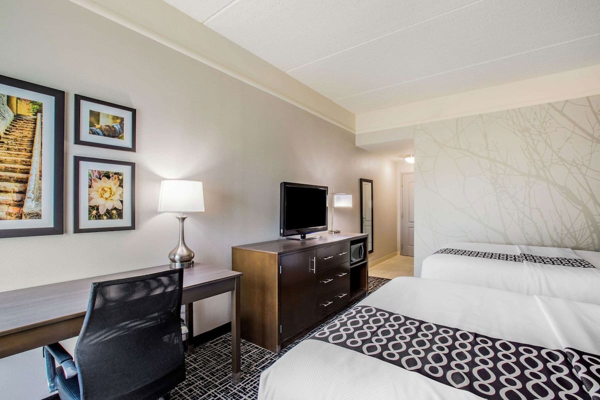 A hotel room with a bed, a desk, a TV, a chair, and framed pictures on the wall.