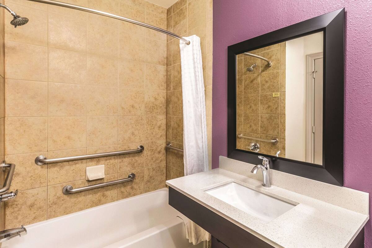 A bathroom with a bathtub, a shower with a handrail, a sink with a mirror, and a towel rack.