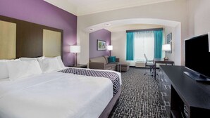 Habitación de hotel con dos camas, un escritorio, un televisor y vistas de la ciudad a través de amplias ventanas.