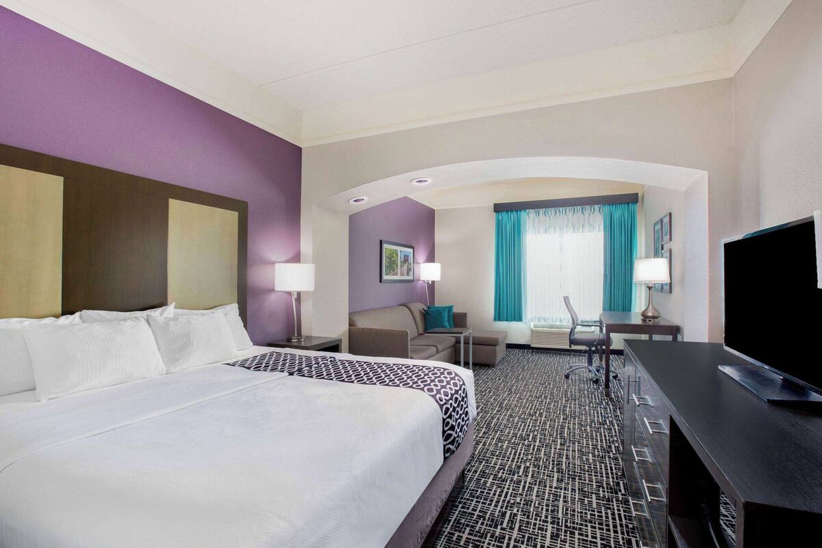 A hotel room with two beds, a desk, a TV, and a view of the city through large windows.