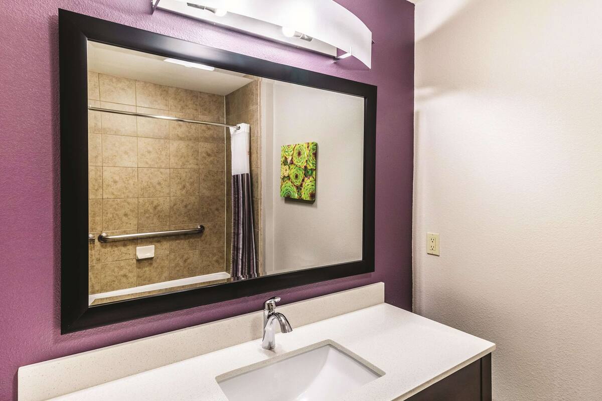 A bathroom with a large mirror, a sink, and a shower area.
