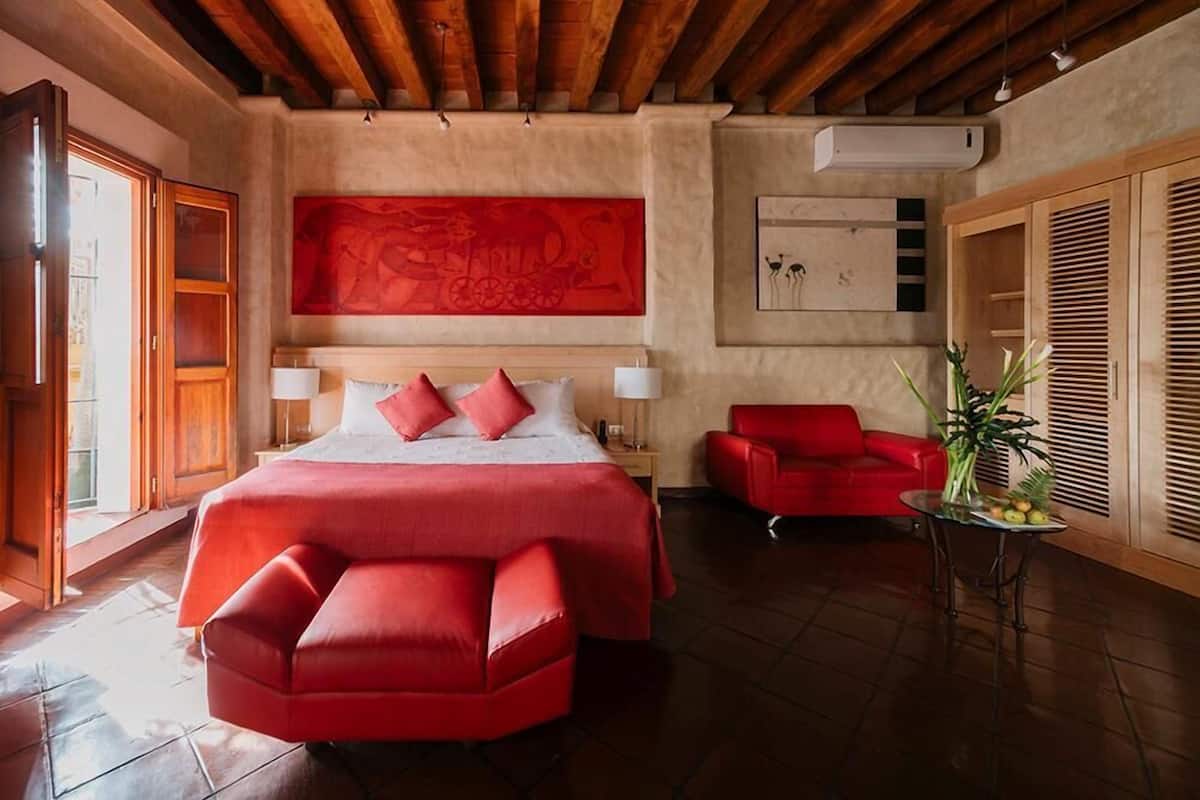 Habitación de hotel con una cama grande, un sofá rojo, una mesita con una planta y una obra de arte roja en la pared.