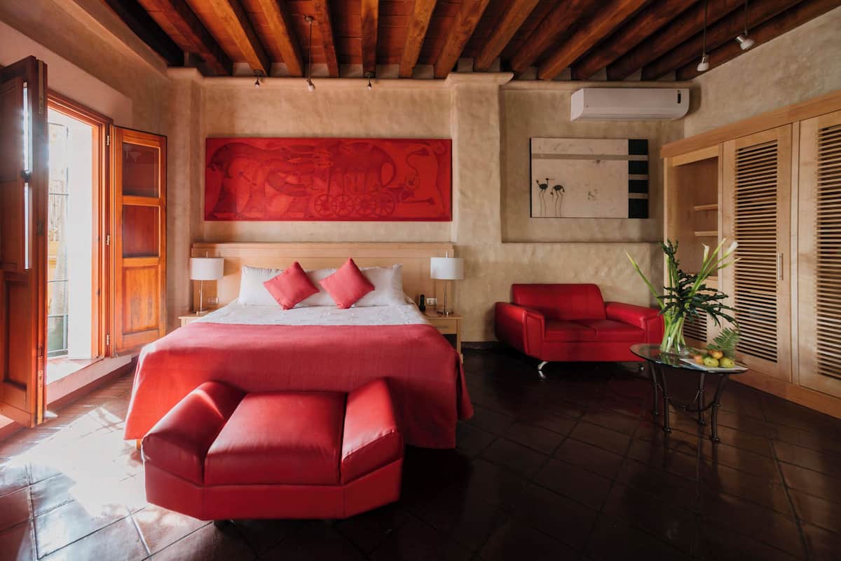 Un dormitorio espacioso con una cama grande, un sofá rojo y una mesita con un florero.