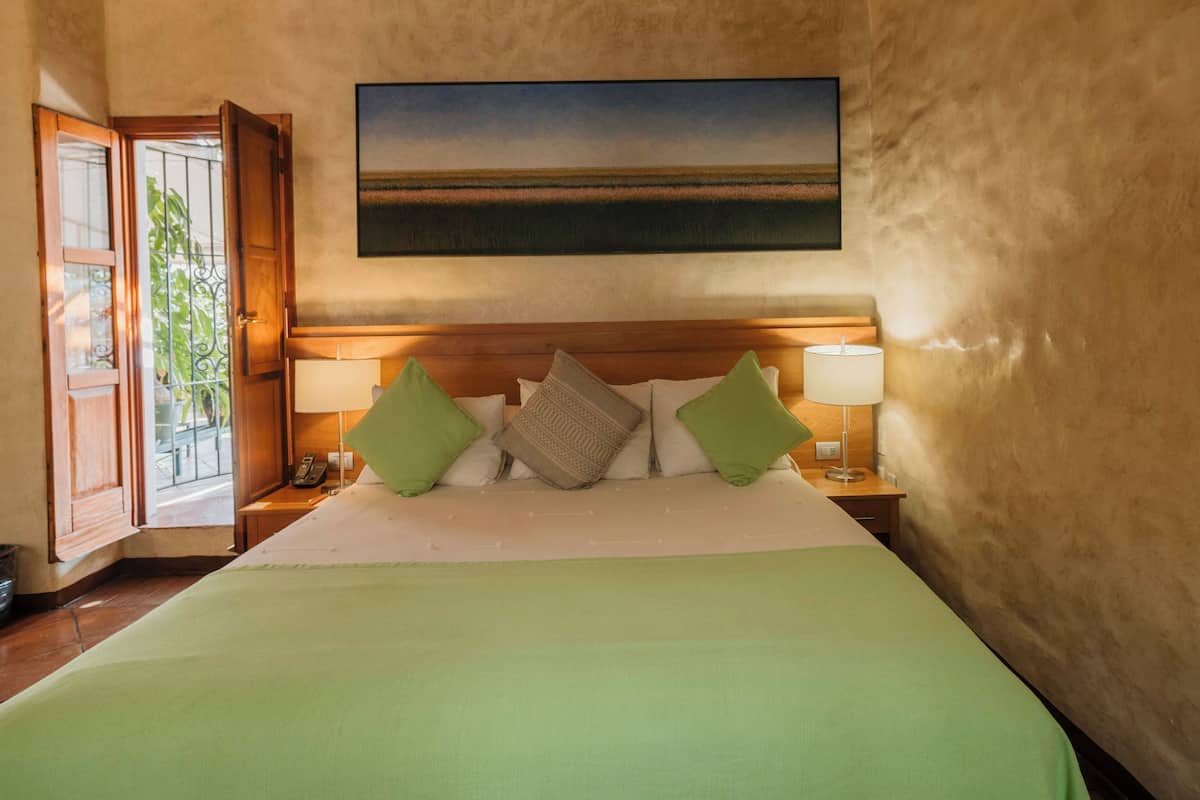Habitación de hotel con una cama grande, dos lámparas de noche, un cuadro sobre la cama y vistas al exterior a través de una puerta.