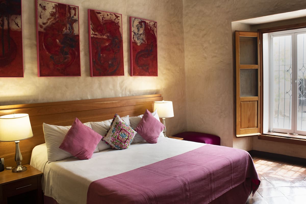 Habitación de hotel con una cama grande, dos lámparas de noche, un cabecero de madera y tres cuadros abstractos en la pared.