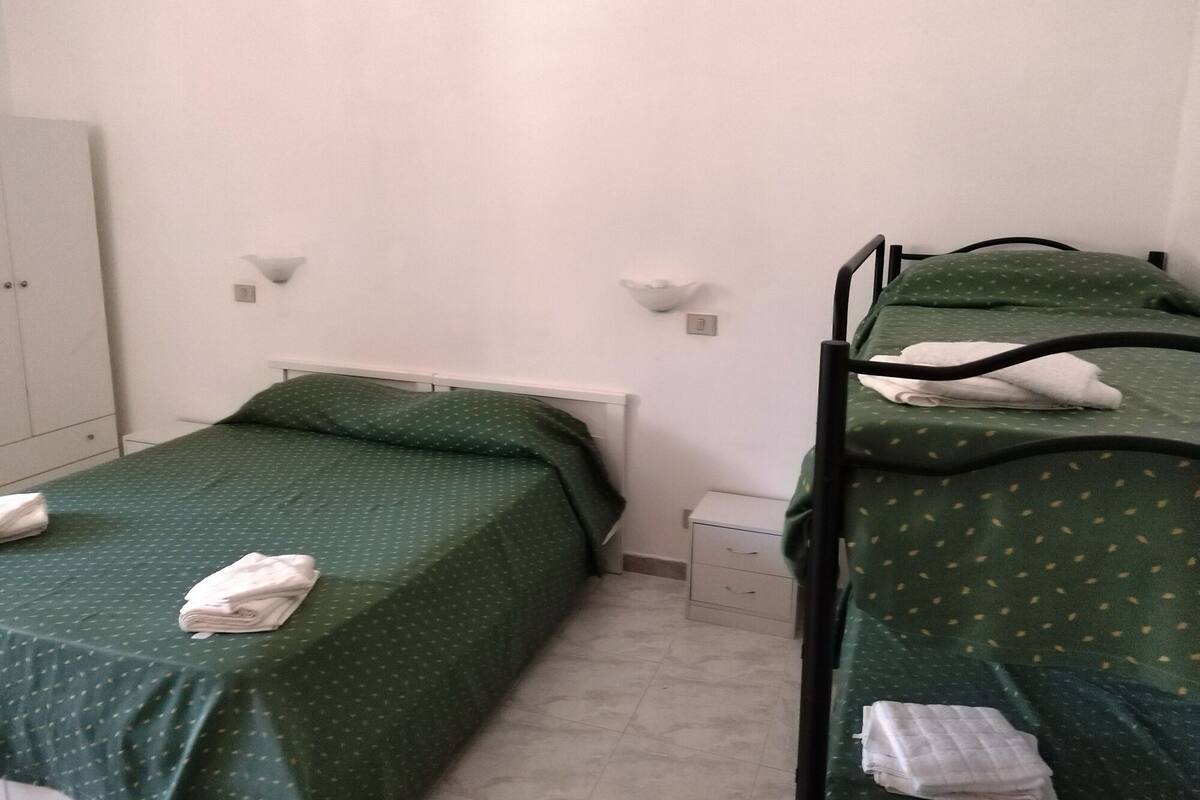 A small, clean room with two bunk beds, a white wardrobe, and a small bedside table.