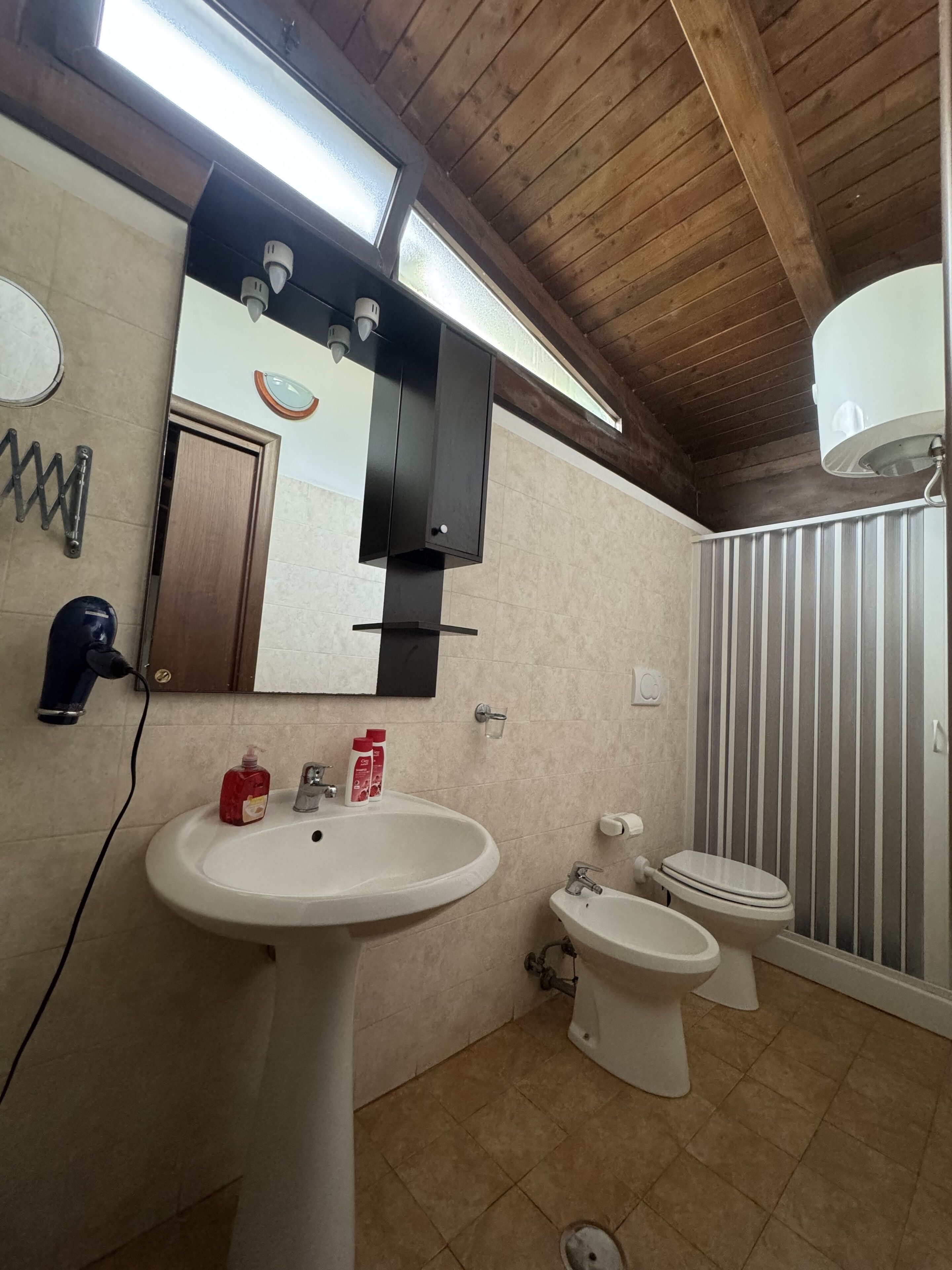 Une salle de bain avec un plafond en bois, un lavabo, des toilettes et un miroir.