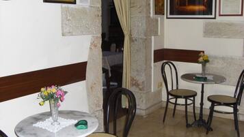 A dining area with round tables and chairs, a vase with flowers, and a wall with framed pictures and certificates.